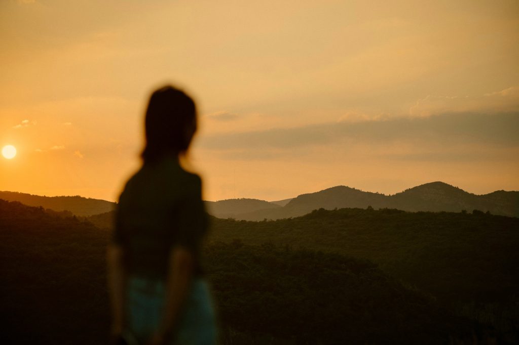A solitary figure standing before mountains at sunset